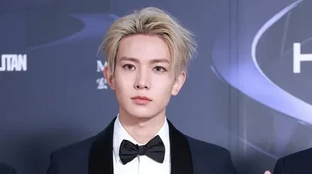 Home 4 Lee Heeseung from ENHYPEN posing in a black tuxedo with blond hair at a red carpet event